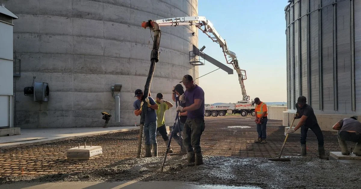 Crew pouring concrete beside grain silos